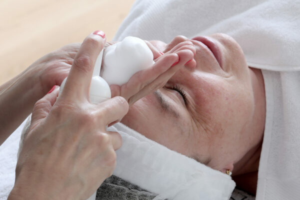 Eine Kosmetikerin trägt einer Kundin einen Reinigungsschaum auf das Gesicht auf.