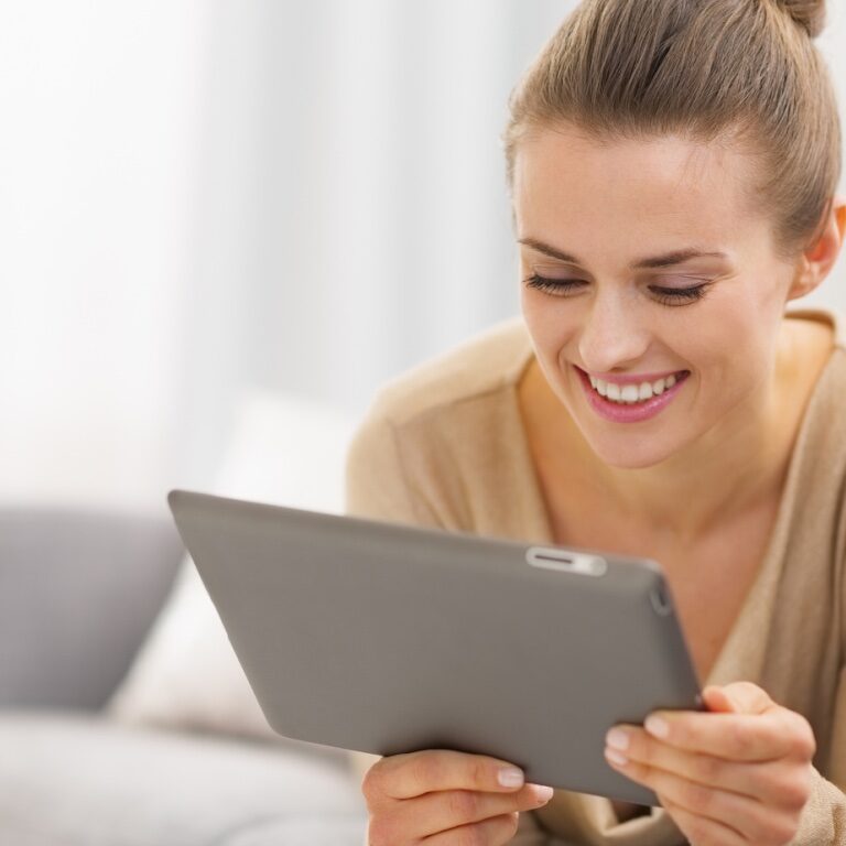 Eine junge Frau die auf den Bildschirm von einem Tablet schaut und lacht.